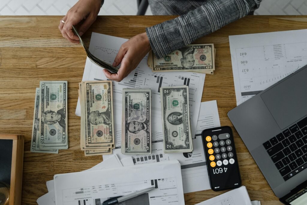 Person counting cash with a calculator and documents on a wooden desk, representing financial planning.